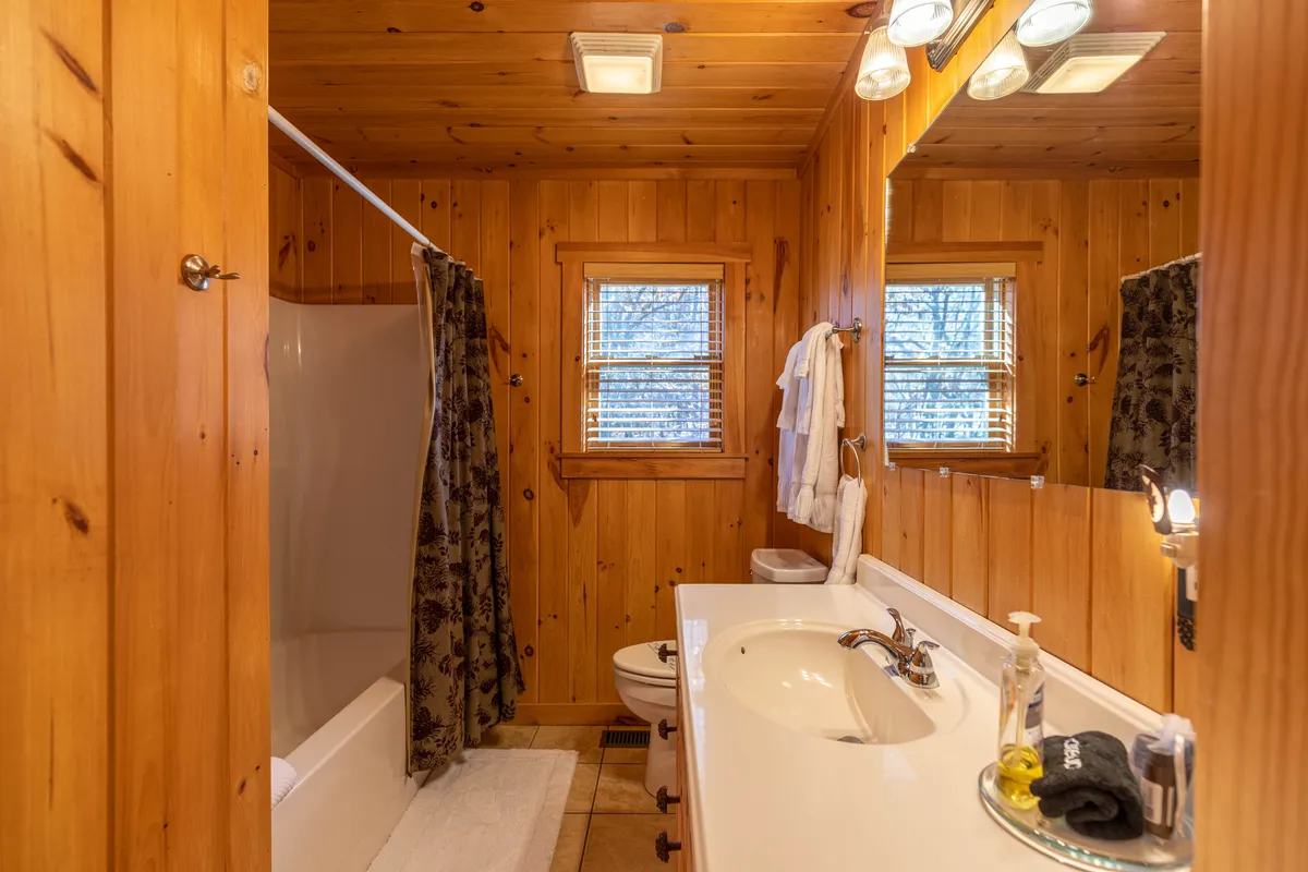 A bathroom with wood-paneled walls, a bathtub/shower combo, a vanity with a sink, a mirrored cabinet, and a window letting in natural light. The design is both functional and soothing, ideal for unwinding after outdoor adventures.