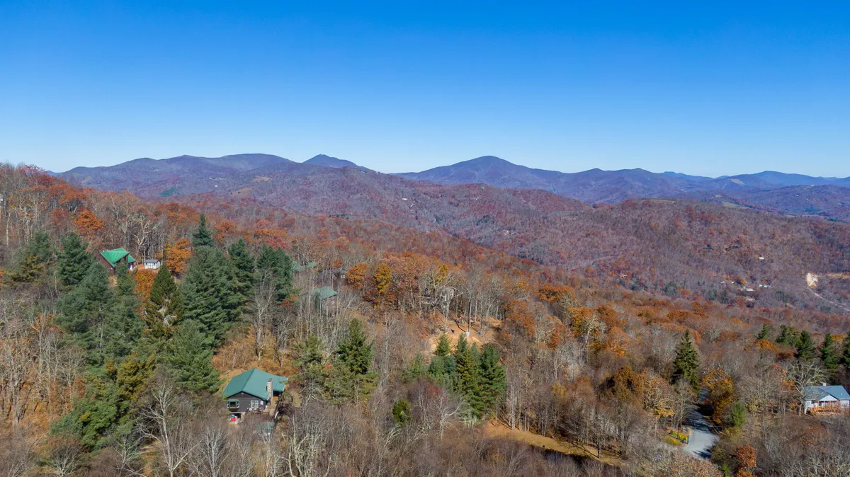 A sweeping view of a lush mountain valley dotted with scattered cabins and dense tree coverage. The scene is peaceful, emphasizing the expansive natural beauty and sense of escape offered by the area.