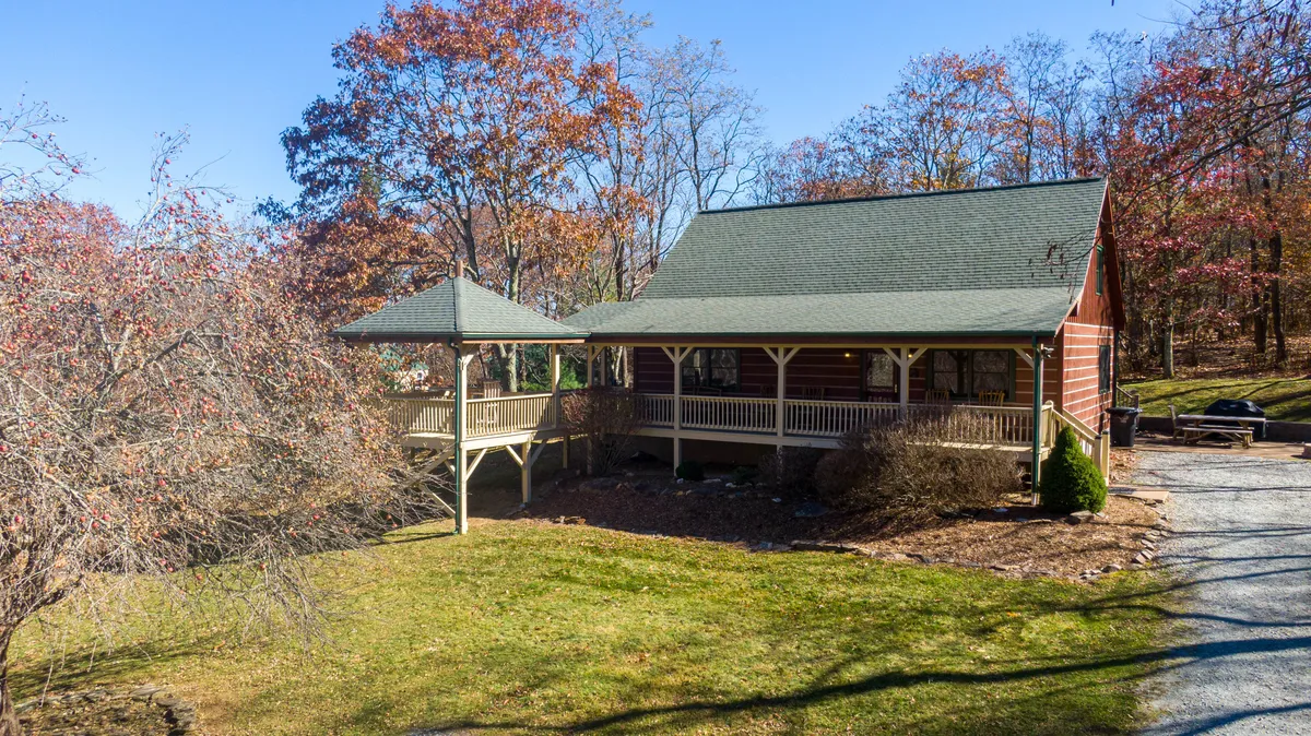 This image captures the inviting exterior of the cabin, showcasing the gated front porch and the gazebo nestled among the surrounding trees. The scene exudes tranquility and the welcoming charm of the entryway, with ample space for relaxing or gathering with loved ones, all set against a backdrop of natural beauty.