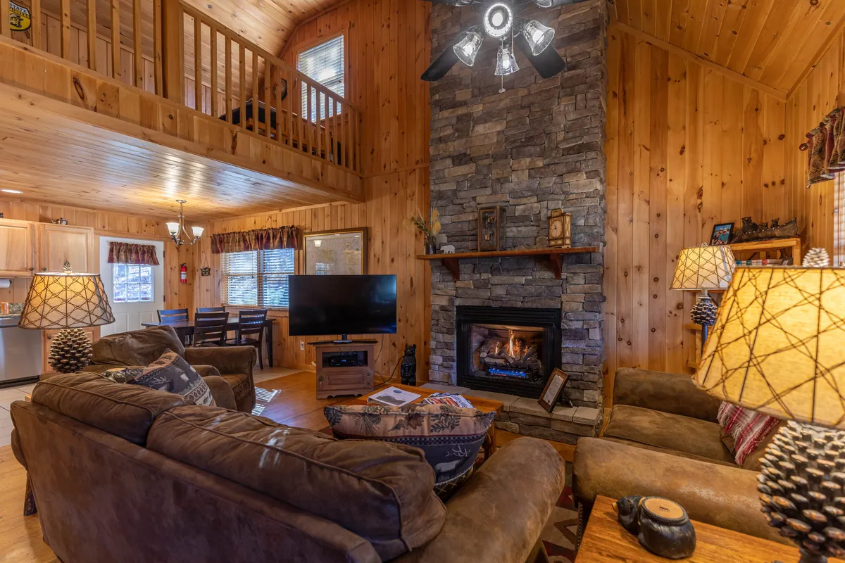 Featuring the great room’s dominant stone fireplace, plush seating, and warm wooden accents, this interior shot creates a sense of coziness and hospitality. The setup is ideal for family time, watching TV, or gathering around the fire—exactly as described in the section content.