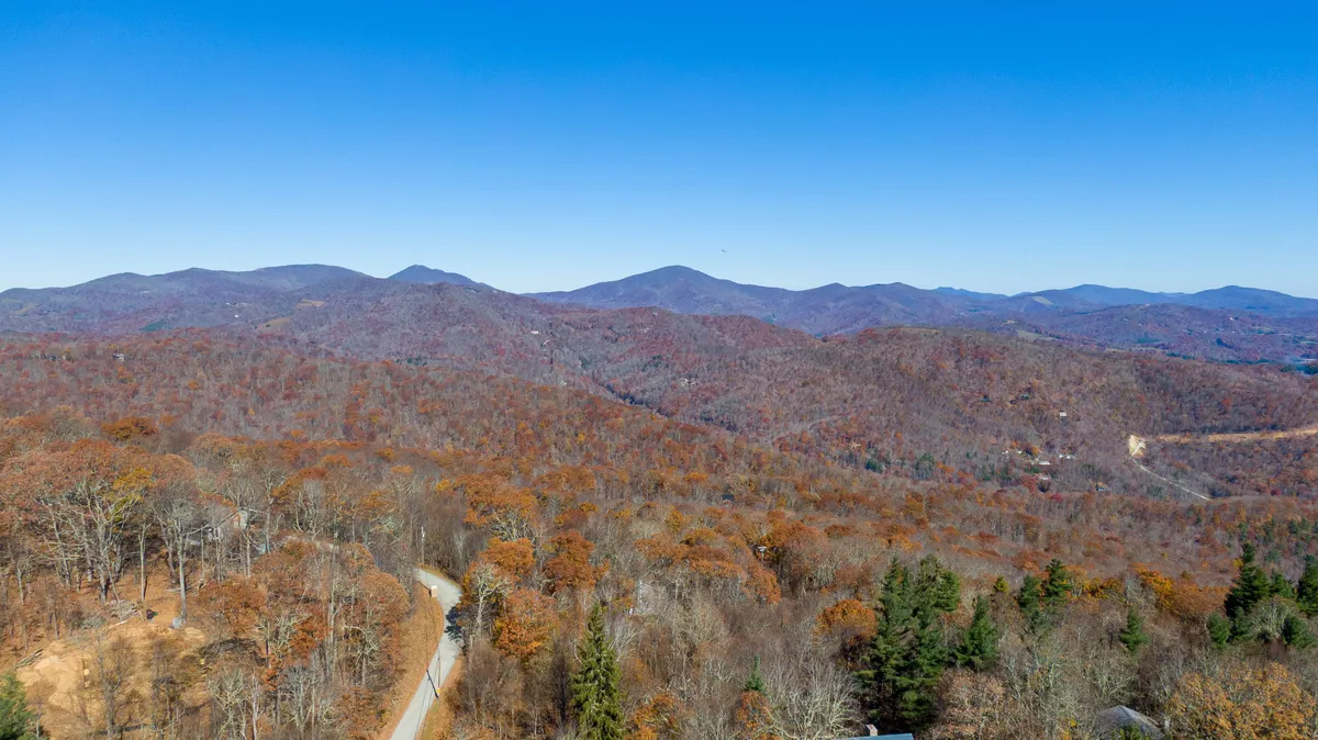 A breathtaking view of a mountain range surrounded by autumn foliage and a winding road, suggesting adventure and exploration in the natural world.