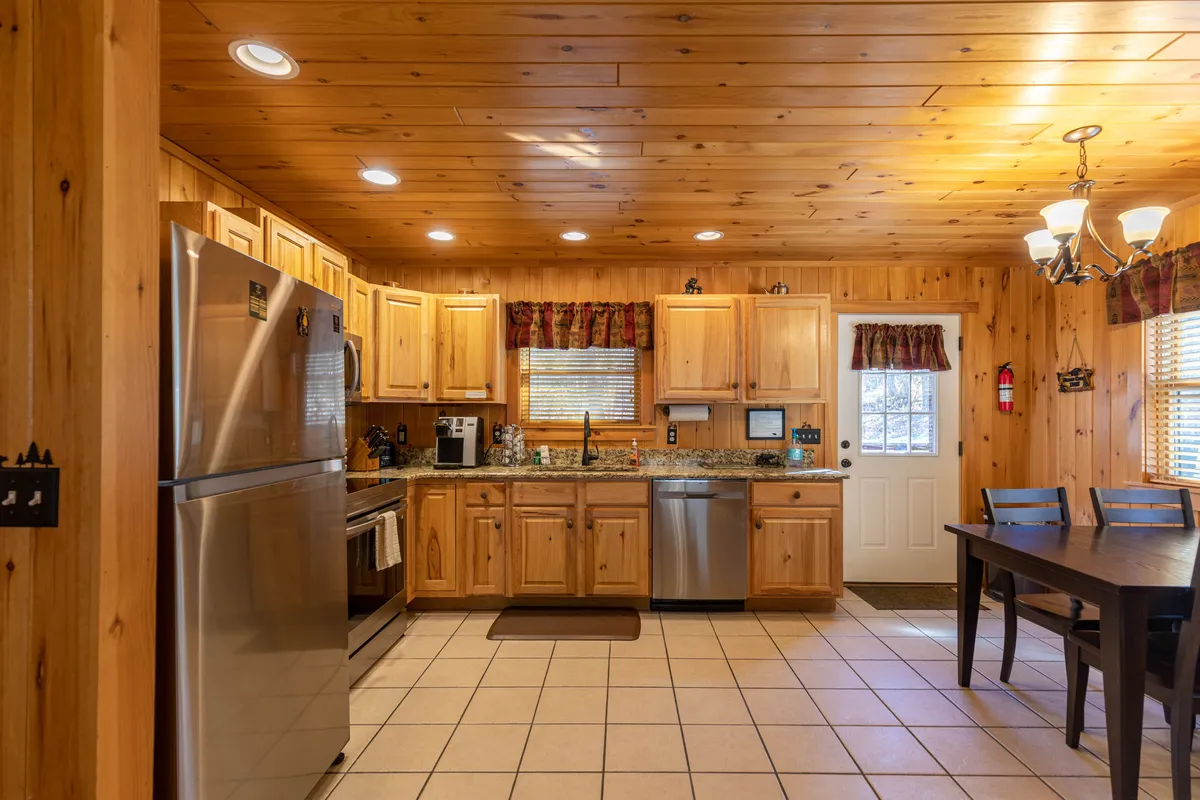 A spacious kitchen and dining area with a kitchen island, stainless steel appliances, wooden cabinetry, and a large dining table. The setting is arranged for group meals and festive gatherings, with warm lighting enhancing the welcoming vibe.