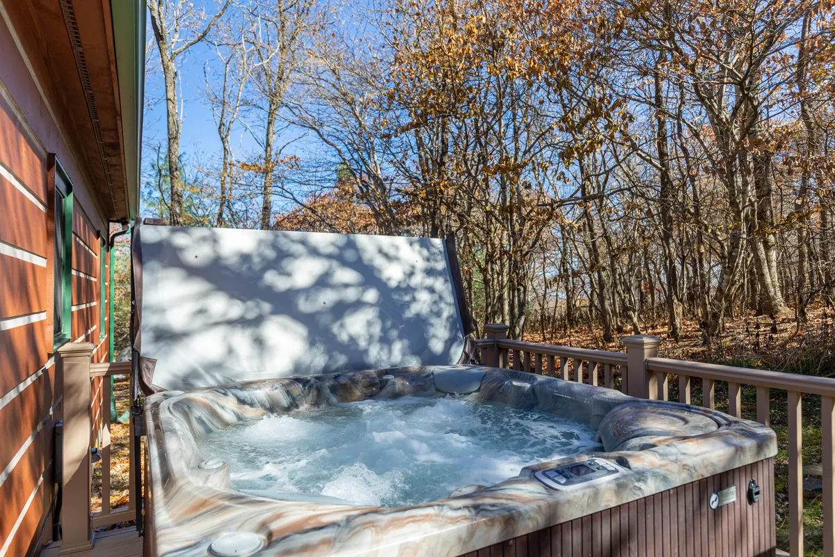 A serene private deck with a bubbling hot tub surrounded by trees and bordered by a wooden railing. The scene evokes relaxation and offers a seamless indoor-outdoor transition, perfect for soaking and stargazing.