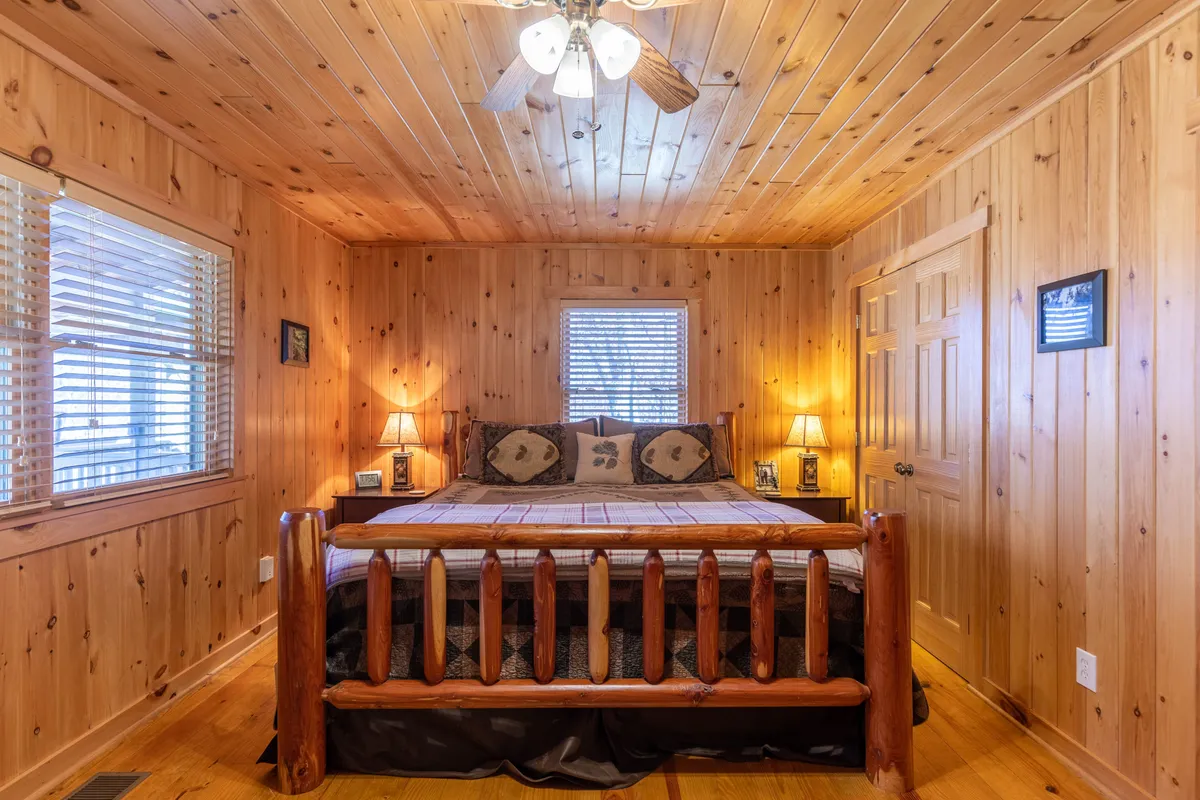 A cozy, warmly lit bedroom featuring a wooden bed, decorative pillows, and wood paneling. Sunlight gently filters through the window, creating an inviting atmosphere perfect for rest and relaxation.