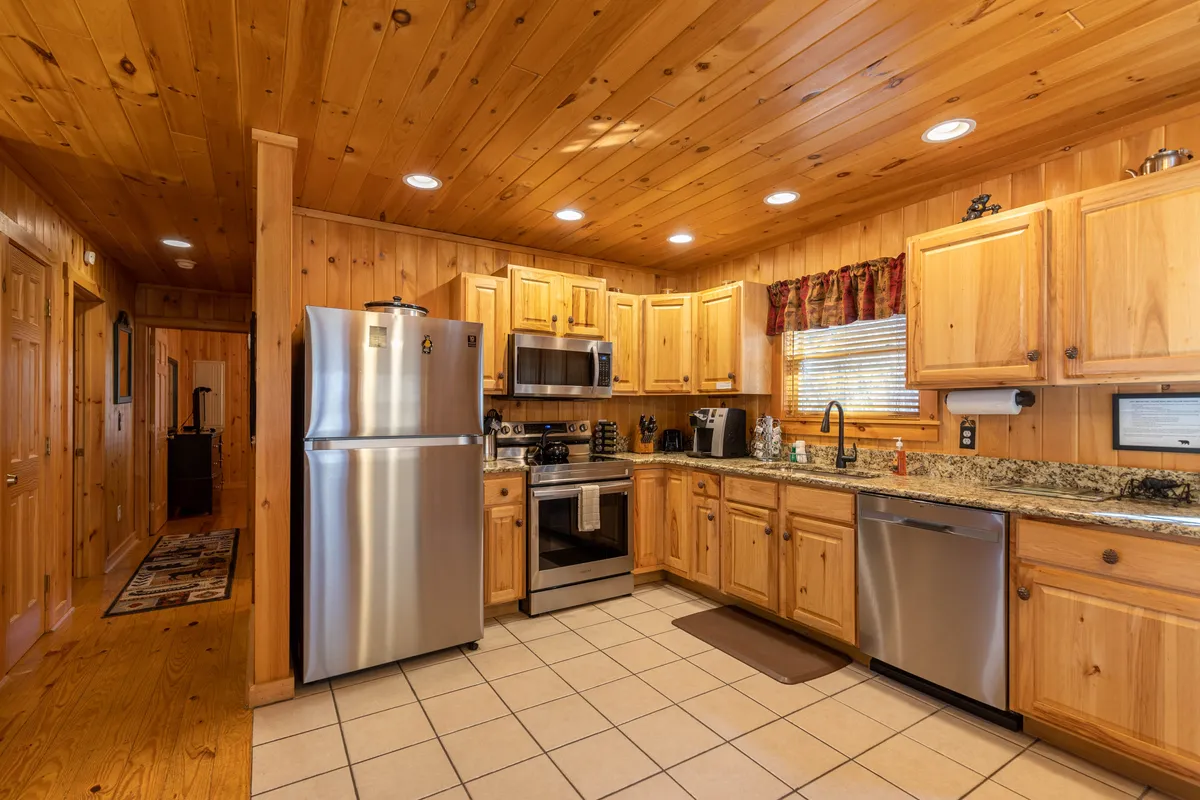 A cozy kitchen featuring stainless steel appliances, a granite countertop, and wooden cabinets. Sunlight streams through a window, illuminating the space and highlighting the inviting atmosphere. The open layout suggests ample room for meal preparation and socializing.