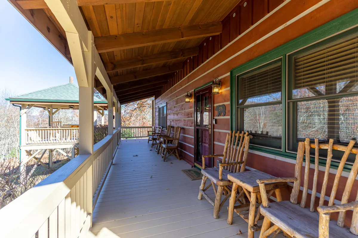 A welcoming porch with wooden rocking chairs and decorative lanterns offers a cozy spot to relax and take in the mountain views. The log cabin exterior and surrounding trees add to the rustic, peaceful ambiance.