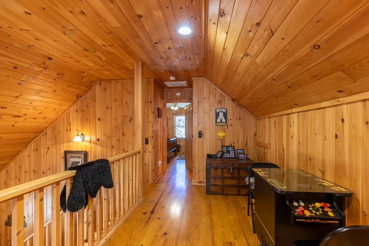 This image features a game loft with wooden railings, an arcade machine, a chest, and artwork on the wall. The space is cozy and inviting, with plenty of room for family members to gather, play games, or relax together.